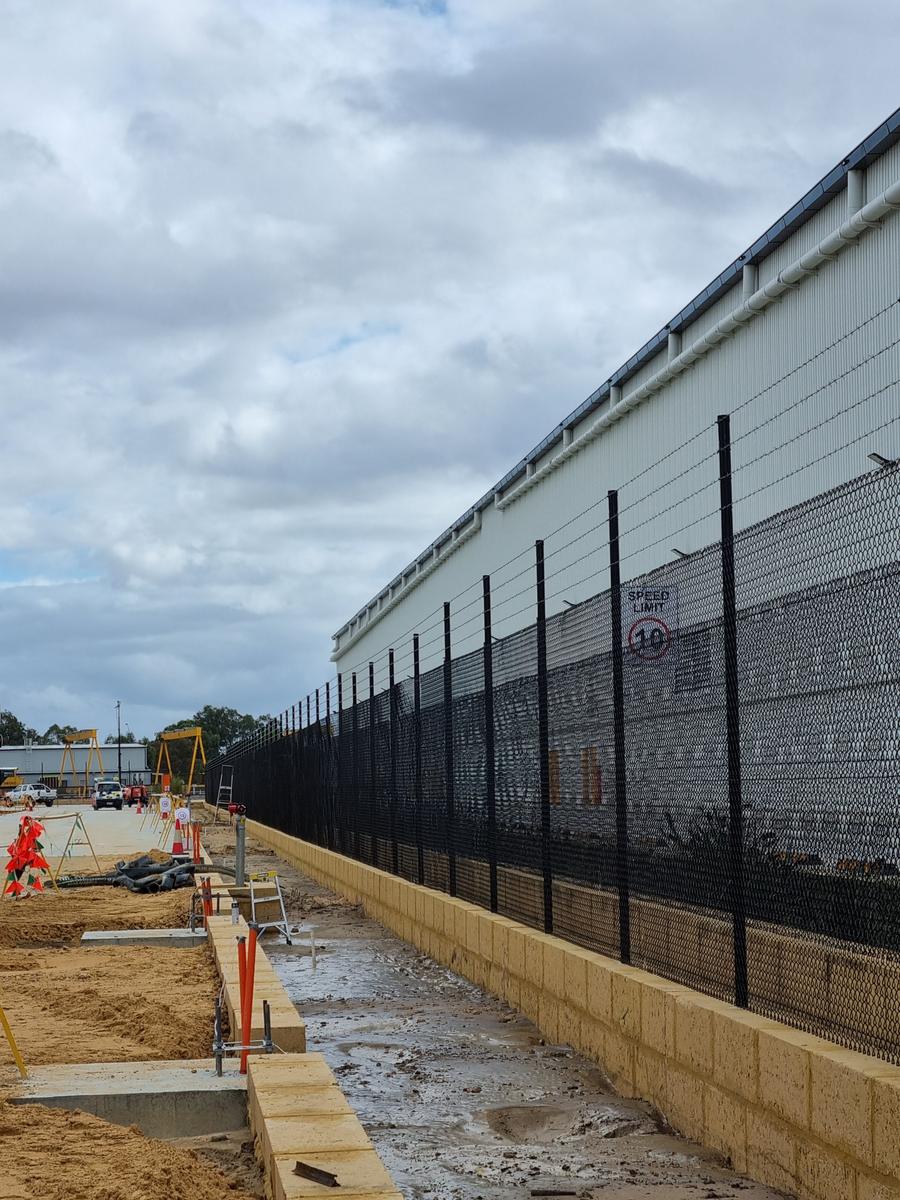 Black chainmesh fence with barbed wire along a warehouse