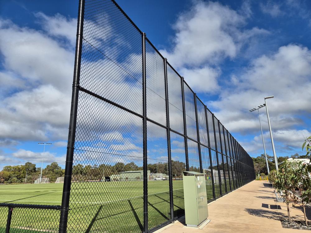 Tall black chainmesh court fencing beside a sports field